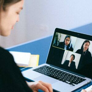 A woman engaging in a video conference using a laptop at home, taking notes.