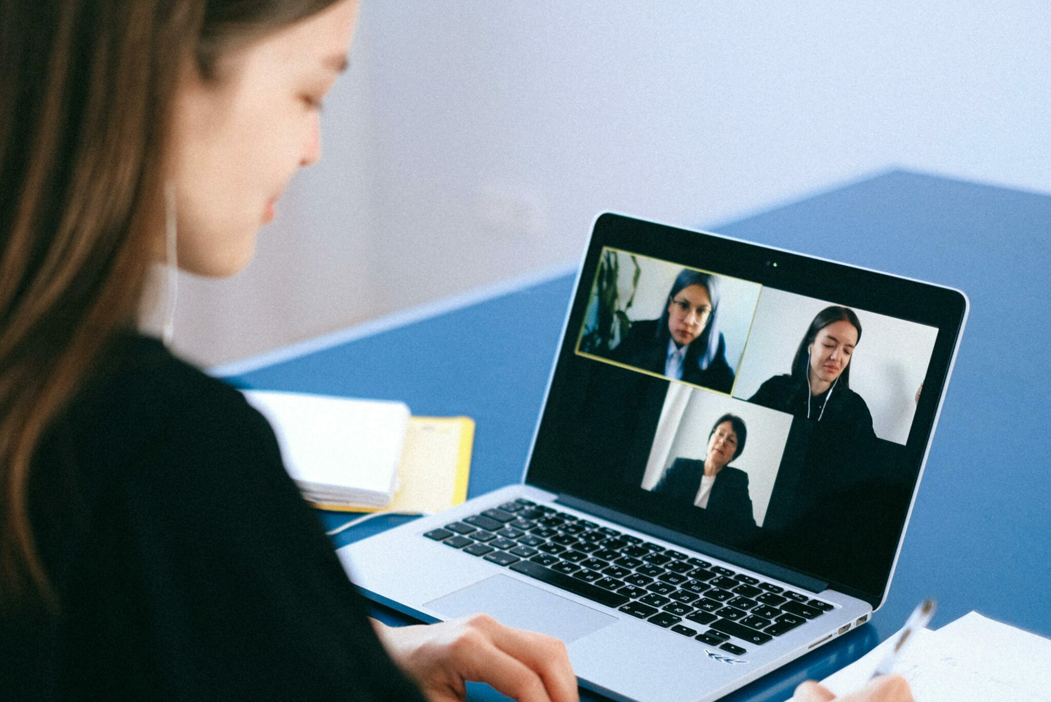 A woman engaging in a video conference using a laptop at home, taking notes.
